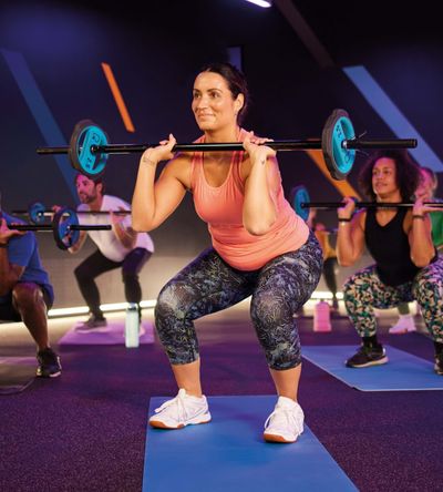 A class session where gyms users are toning their muscles by doing squats with a weighted crossbar.